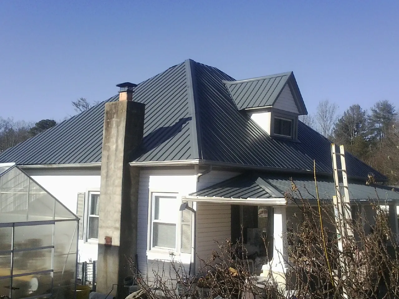 Dark blue standing seam metal roof on a white farmhouse with dormer — Slate & Tile Roof Repair by Roofing Brothers in Guntown