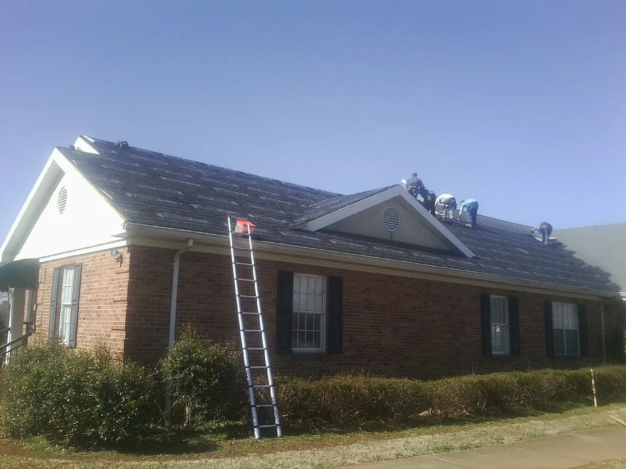 Crew tearing shingles off a brick ranch roof with a ladder set — Emergency Roof Repair work by our crew in Guntown