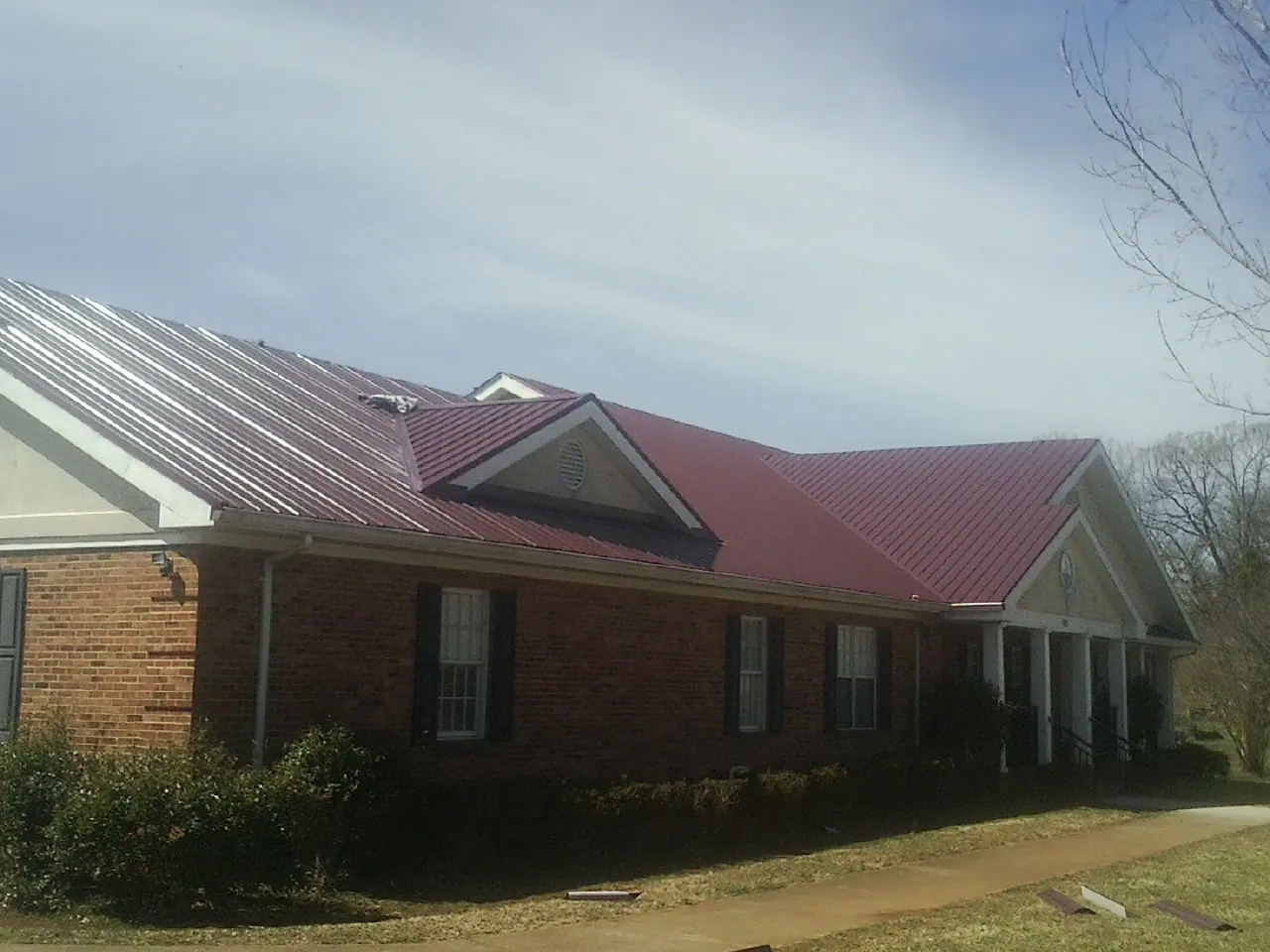Red metal roof with gabled entries on a long brick building, from a Hail Damage Roof Repair job in Guntown