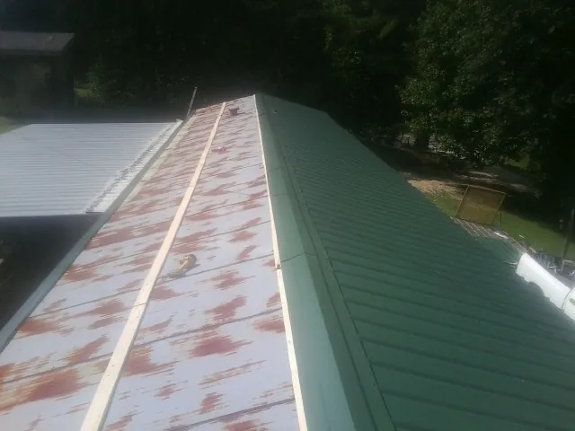 Old rusted panels beside newly installed green metal roofing — Wind Damage Roof Repair by Roofing Brothers in Guntown