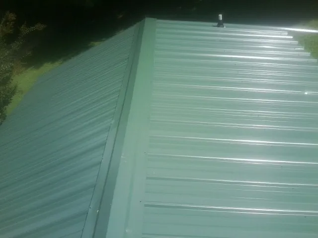 New green metal panels meeting at the ridge of a roof — Flat Roof Repair work by our crew in Guntown