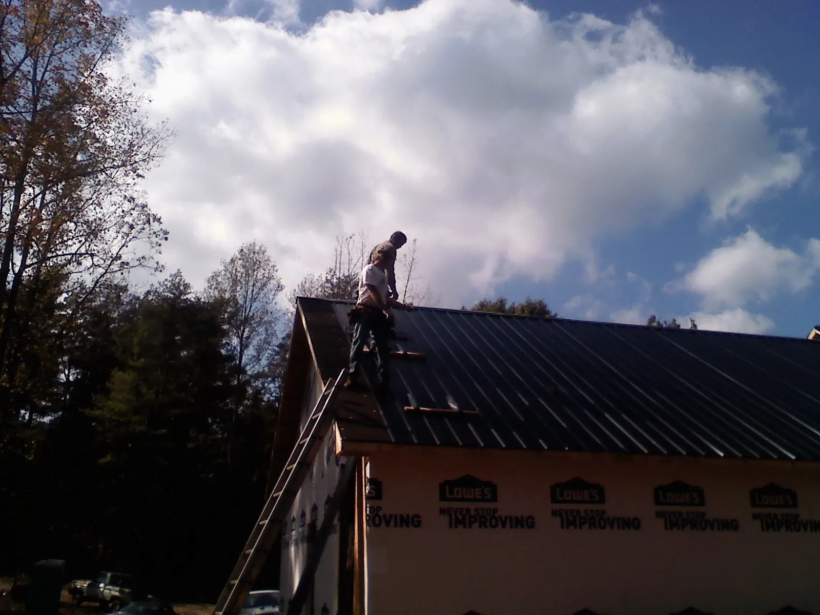 Roofer fastening dark metal panels high against a cloudy sky, from a Roof Inspection job in Guntown