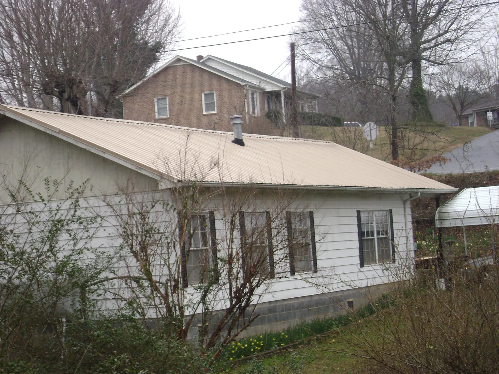 Tan metal roof on a white sided house set into a hillside — Commercial Roofing by Roofing Brothers in Guntown